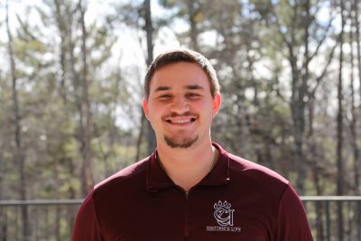 A photo of Caleb Dangerfield against a sunny wooded backdrop.