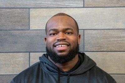 A photo of Jairus Marlow standing in front of a gray slate tile wall.