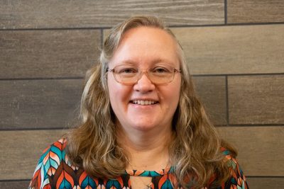 A photo of Bonnie Catron standing in front of a gray slate tile wall.