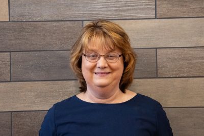 A photo of Print Shop Supervisor, Lisa Neel, standing in front of a slate tile wall.